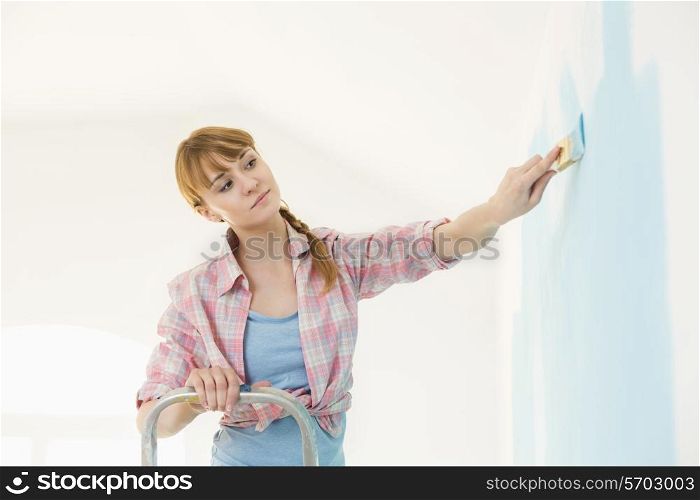 Woman on ladder painting wall with paintbrush