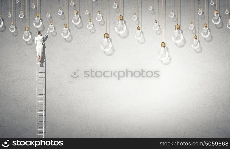 Woman on ladder top. Back view of businesswoman standing on ladder and reaching light bulb