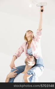 Woman on man&rsquo;s shoulders painting ceiling with paint roller