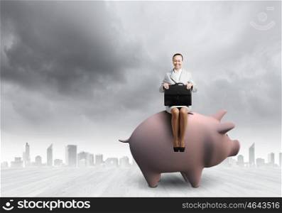Woman on moneybox. Young businesswoman with suitcase in hand sitting on piggybank
