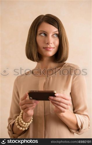 Woman on phone texting text message on smartphone app standing indoor on trendy background. Cool young modern female model in her 20s.
