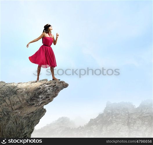 Woman on rock edge. Young woman in red dress wearing black blindfold