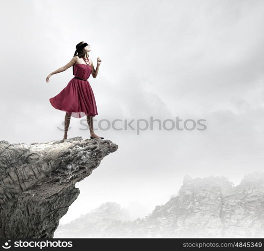 Woman on rock edge. Young woman in red dress wearing black blindfold