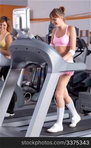 Woman on running machine in gym with her friend.