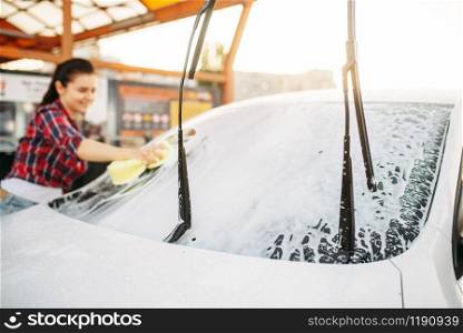 Woman on self-service car wash, carwash process. Outdoor vehicle washing at summer day. Female person with sponge cleans automobile front glass. Woman on self-service car wash, carwash process