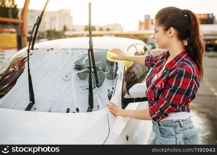 Woman on self-service car wash, carwash process. Outdoor vehicle washing at summer day. Female person with sponge cleans automobile front glass