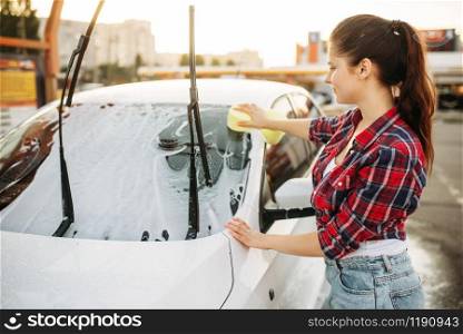 Woman on self-service car wash, carwash process. Outdoor vehicle washing at summer day. Female person with sponge cleans automobile front glass