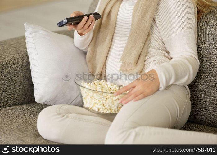woman on sofa holding television remote control and popcorn