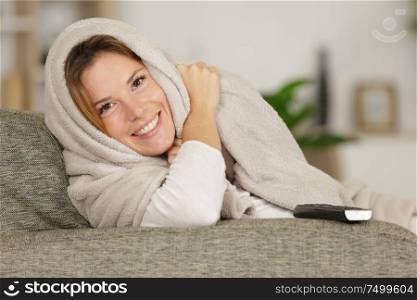 woman on sofa wrapped in blanket watching television