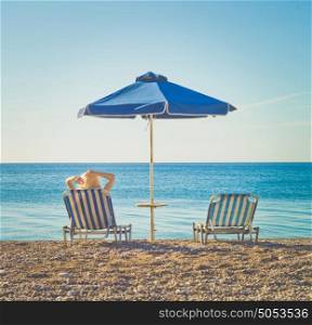 Woman on southern beach resting in a chaise-longue under an umbrella. Summer travel. Beach vibes