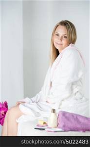 Woman on spa or massage sitting on table and waiting for masseur wearing bathrobe