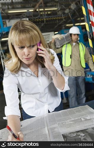 Woman on telephone checking newspapers in factory