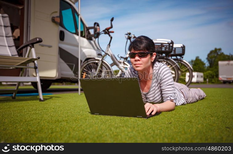 Woman on the grass, looking at the laptop near the camping . Caravan car Vacation. Family vacation travel, holiday trip in motorhome