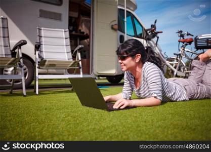 Woman on the grass, looking at the laptop near the camping . Caravan car Vacation. Family vacation travel, holiday trip in motorhome