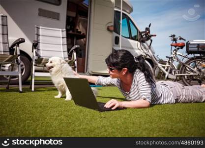 Woman on the grass with a dog looking at a laptop. Caravan car Vacation. Family vacation travel, holiday trip in motorhome