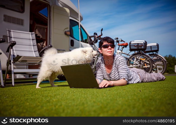 Woman on the grass with a dog looking at a laptop. Caravan car Vacation. Family vacation travel, holiday trip in motorhome