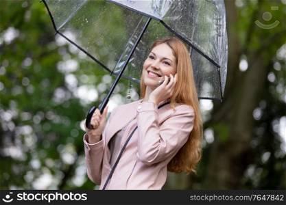 woman on the phone holding umbrella out in the rain