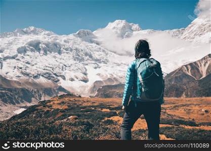 Woman on the stone and mountain valley. Standing young woman with backpack on the stone and looking on snow covered mountains in clouds at sunset. Landscape with girl, high rocks with snowy peaks, yellow grass, blue sky in Nepal. Travel