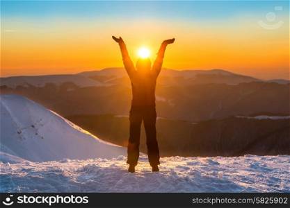 Woman on the top of winter mountain holding sun in her hands