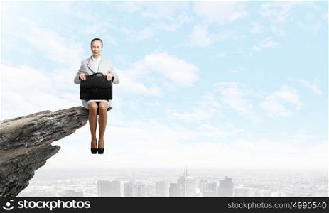 Woman on top. Young pretty businesswoman sitting on top of rock high above city