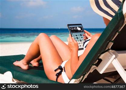 Woman on vacation lies in a sun lounger on the beach with a tablet in hands (copy space display).