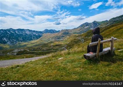 Woman on wooden bench is looking at picturesque summer mountain landscape of Durmitor National Park, Montenegro, Balkans Dinaric Alps, UNESCO World Heritage. Durmitor panoramic road, Sedlo pass.