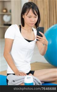 woman on yoga mat looking at smartphone