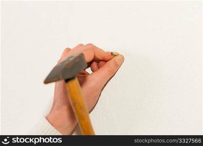 Woman - only hand to be seen - is driving a nail into a wall in her house
