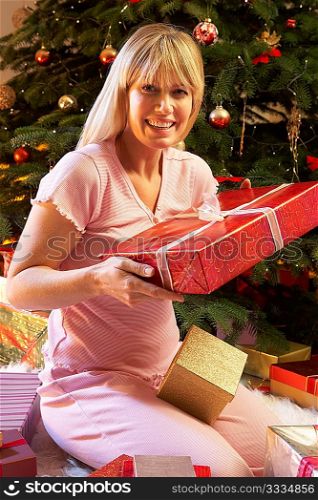 Woman Opening Christmas Present In Front Of Tree