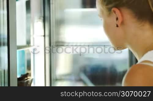 Woman opening fridge at the shop and taking small chocolate cake