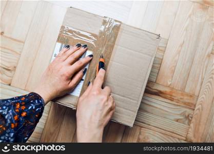 Woman opening parcel online order. Unpacking box with ordered items. Online shopper opening delivered parcel. Delivery service concept