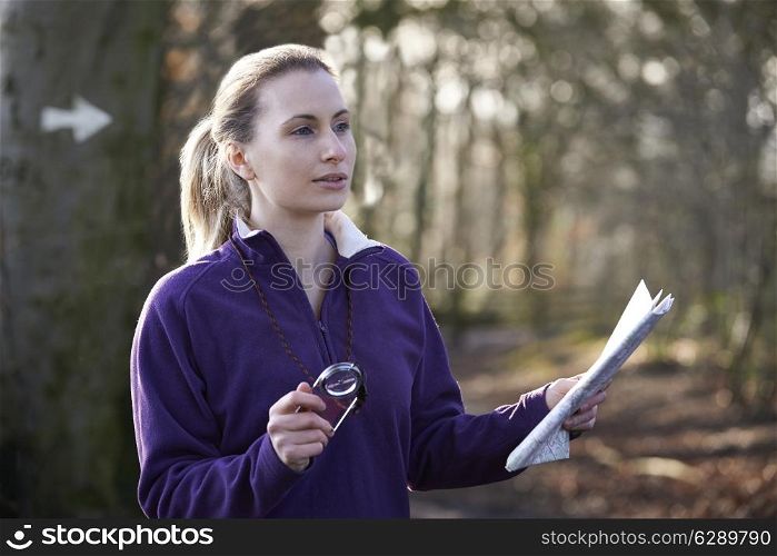 Woman Orienteering In Woodlands With Map And Compass