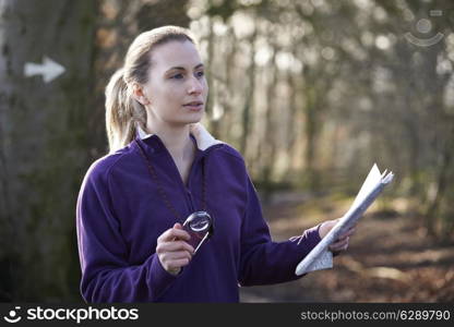 Woman Orienteering In Woodlands With Map And Compass