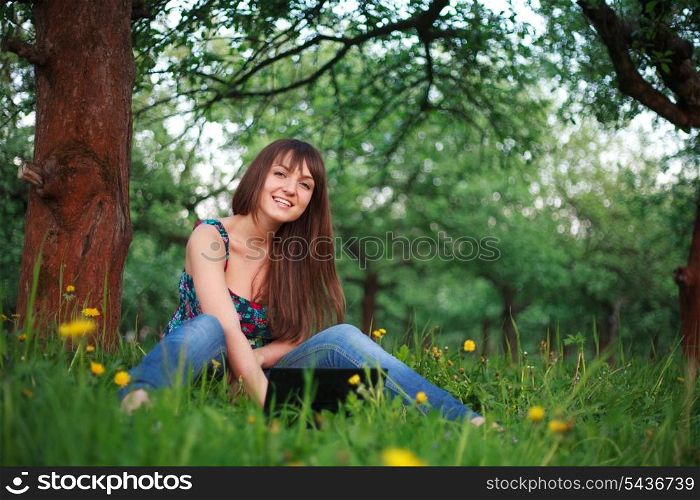 Woman outdoor sitiing with netbook and smiling