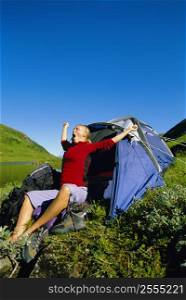Woman outdoors at campsite by lake yawning and stretching