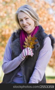 Woman outdoors at park holding leaves in hand smiling (selective focus)