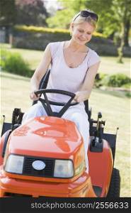 Woman outdoors driving lawnmower smiling
