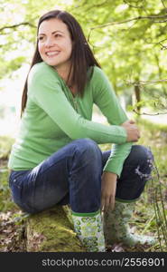 Woman outdoors in woods sitting on log smiling