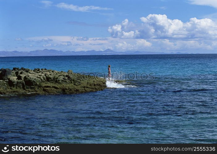 Woman outdoors standing on large rocks Oceanside (far away)