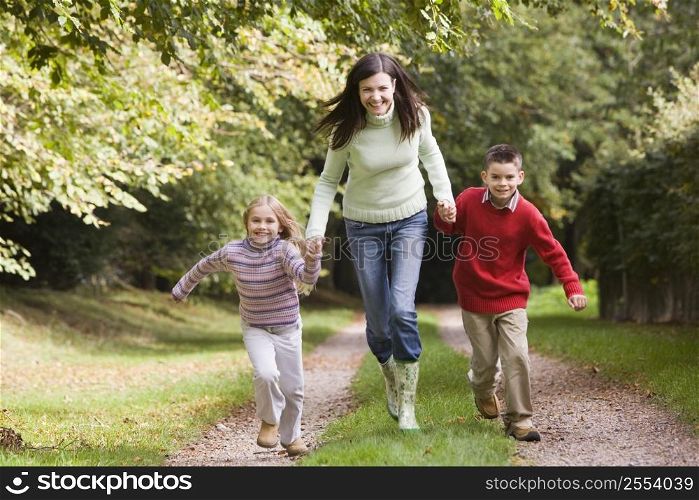 Woman outdoors with two young children walking on path holding hands and smiling (selective focus)