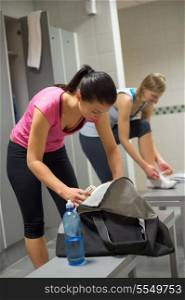 Woman packing bag at gym&rsquo;s locker room with friend in background