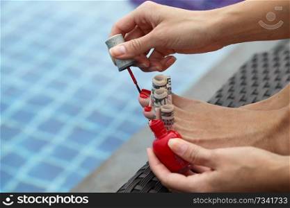 Woman painting nails using dollar bills sitting outdoors by the pool. Rich woman painting nails