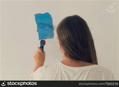 Woman painting wall of her house, do it yourself home renovation concept. Woman painting wall