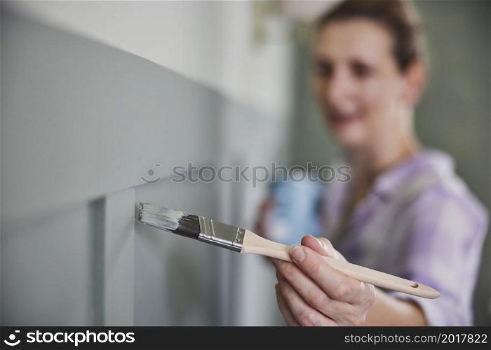 Woman Painting Wall With Panelling In Room Of House With Paint Brush