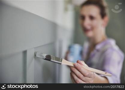 Woman Painting Wall With Panelling In Room Of House With Paint Brush