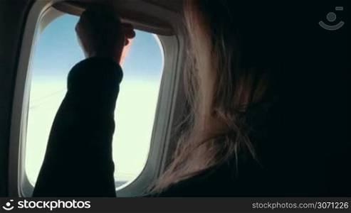 Woman passenger opening the blind and looking out the window of airplane