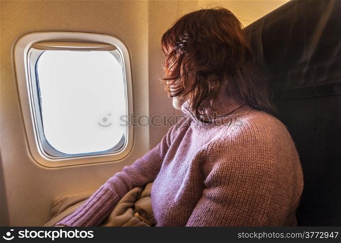 Woman passenger tourist looking through the window of airplane. Travel and tourism.