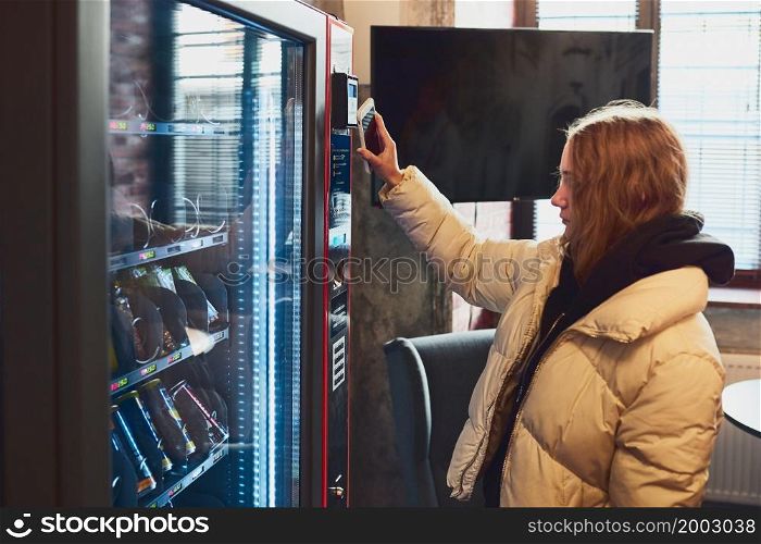 Woman paying for product at vending machine using contactless method of payment with mobile phone. Woman using new way of payments