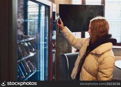 Woman paying for product at vending machine using contactless method of payment with mobile phone. Woman using new way of payments