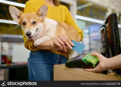 Woman paying for purchase at pet shop using credit card. Closeup view on corgi dog in female customer hand. Closeup woman paying for purchase at pet shop using credit card